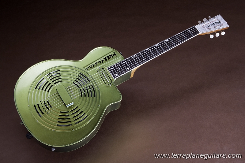 Emerald_City_Centerfold-2.jpg - The Terraplane has a very different string anchoring system. No tailpiece is present to vibrate and rattle against the coverplate. This system puts greater string tension against the bridge saddle for increased tone and volume. A unique pickup raising-lowering system allows the instrument to be used in either an acoustic or electric mode.